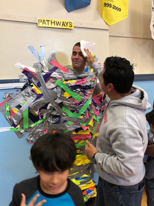 A Teacher Mopping the Brow of a Principal Duct Taped to a Wall