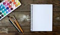 Art supplies on a table with a drawing notebook