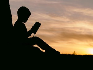 Silhouette of child sitting behind tree during sunset